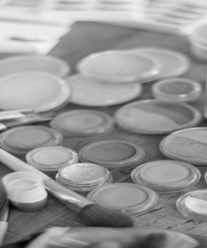 Faded background image of several palettes of foundation and other types of makeup.