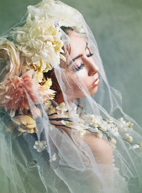Female model looking away from camera wearing white veil and dramatic floral headpiece.