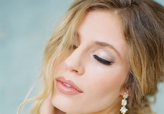 Close up of an attractive blond girl wearing earrings.  She has her eyes closed and is wearing makeup.