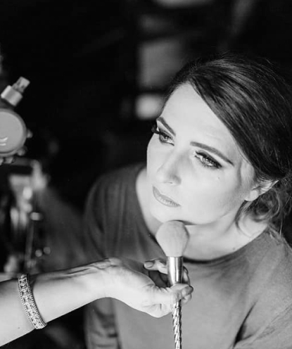 Faded background image of a girl looking away from the camera while someone uses a makeup brush on her face.