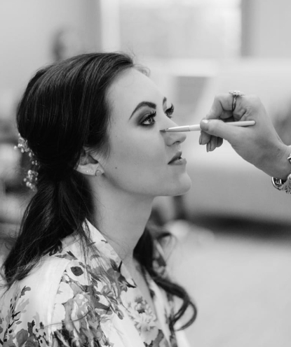 Faded background image of a girl looking away from the camera while someone puts mascara on her.